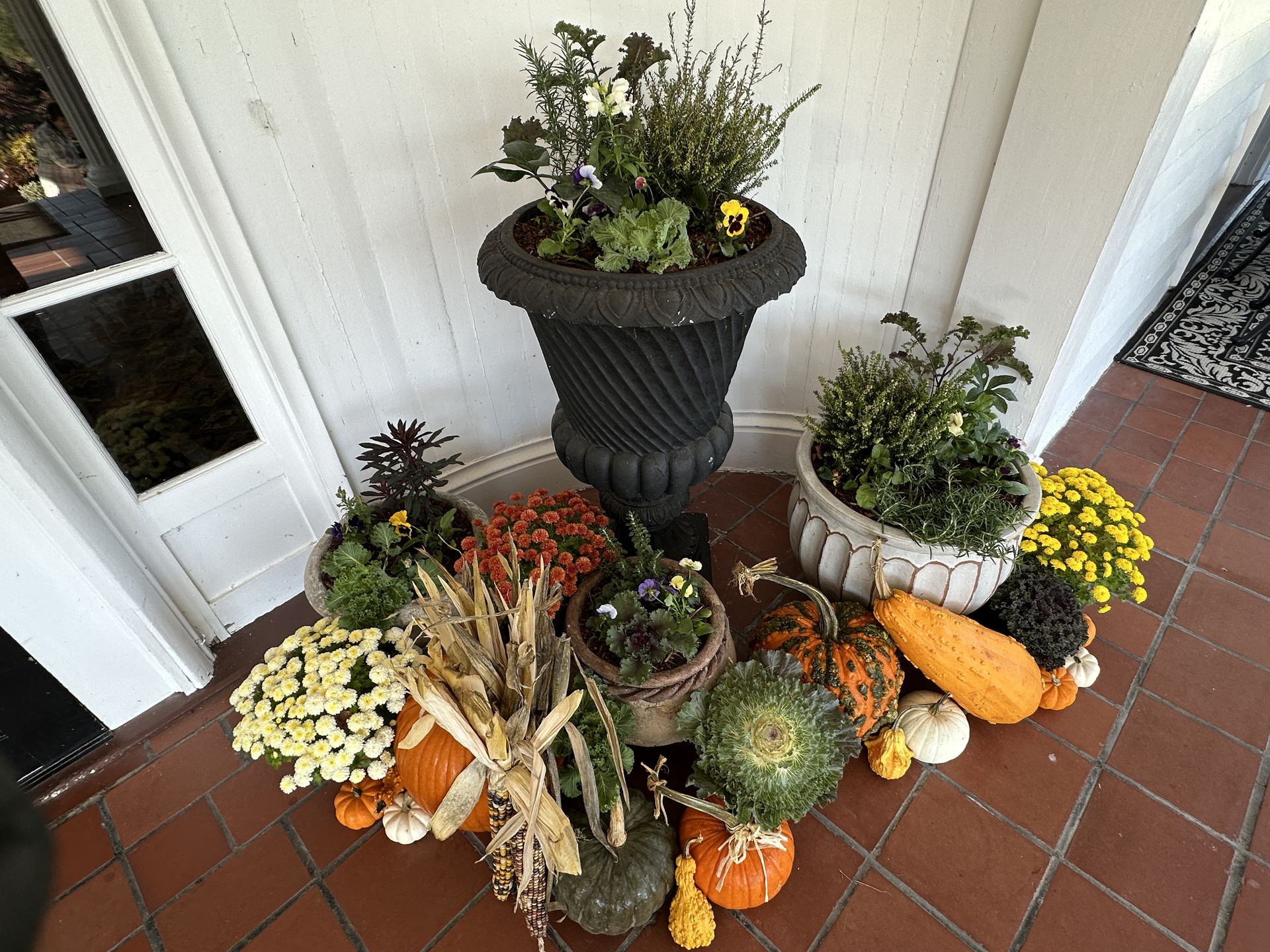 Fall entrance with cool-season planters, ornamental cabbage, mums, pumpkins, gourds, and corn