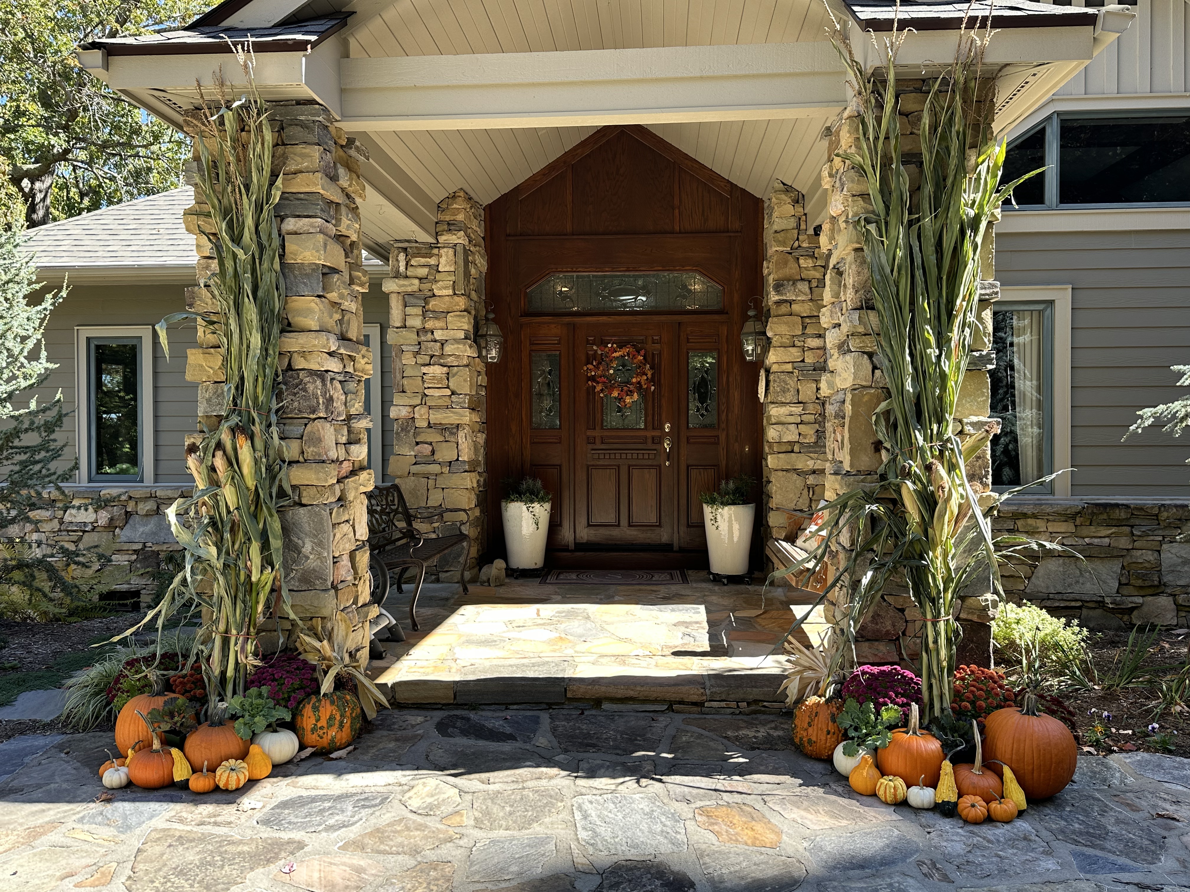 Stone entryway layered with pumpkins, mums, and corn stalks styled for a festive fall welcome